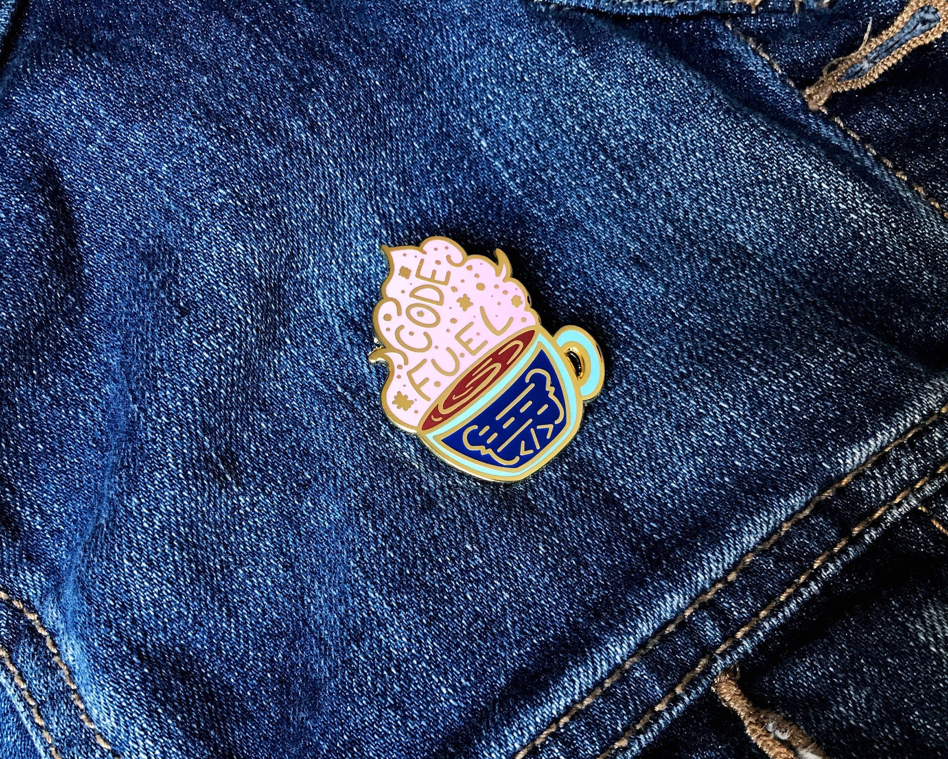 Enamel pin of a coffee cup with a heart on denim fabric