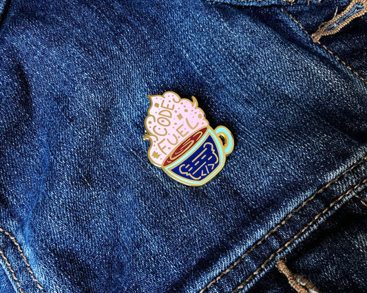 Enamel pin of a coffee cup with a heart on denim fabric